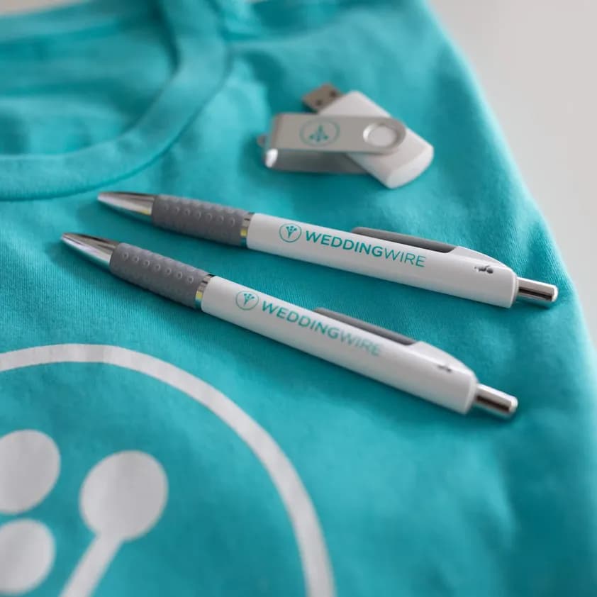 Custom branded WeddingWire pens, USB drive, and teal t-shirt with company logo.