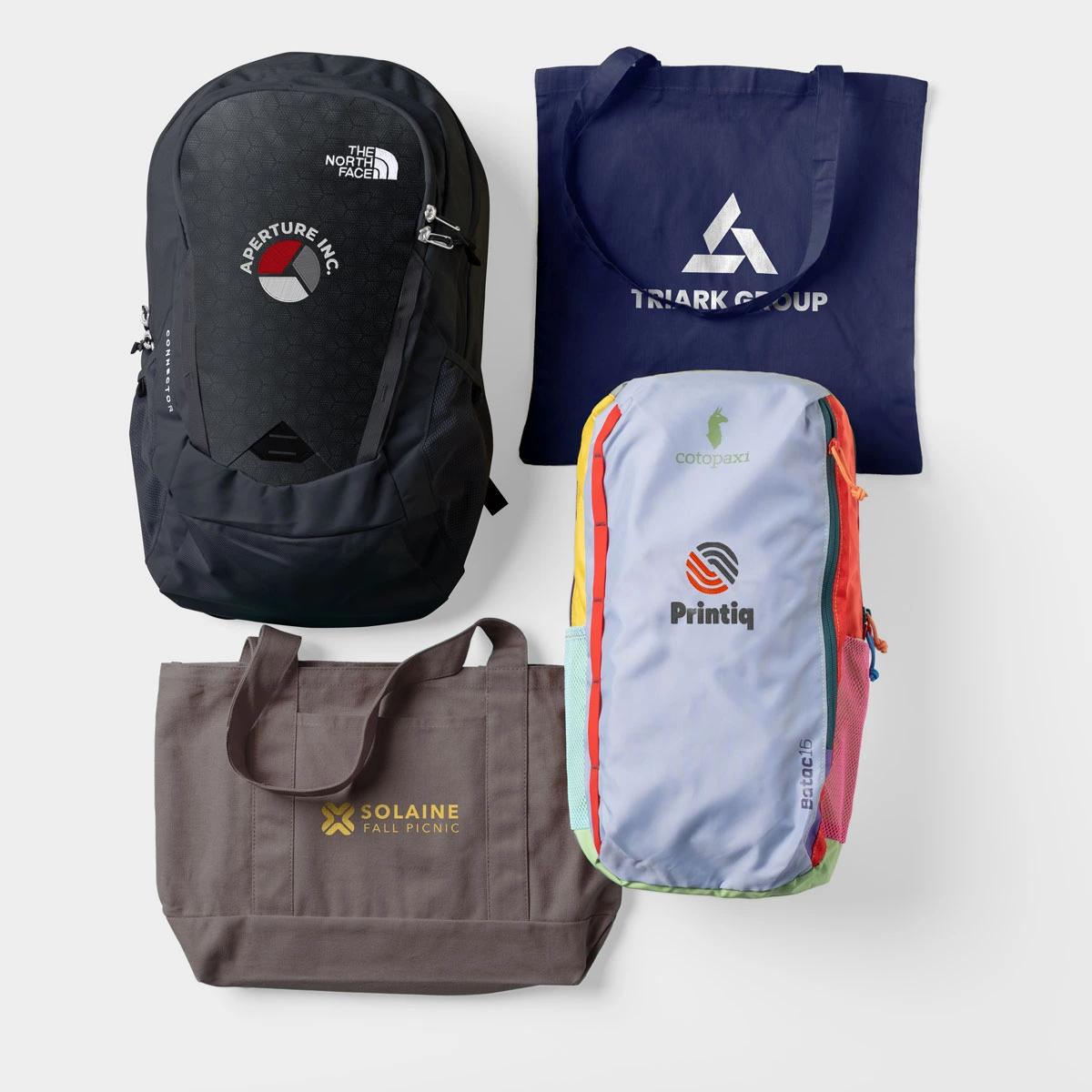Two backpacks and two tote bags are decorated with company logos